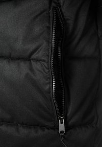 Čierna vypchávkovaná bunda s viditeľnou zipsovou kapsou, vyrobená z textúrovanej látky s hladkým povrchom. Zips je tmavý a kovový.