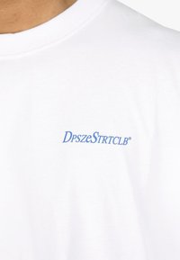 White cotton t-shirt featuring blue text "DpszeStrtclb" on the front. Rounded neckline, short sleeves, and a smooth texture.