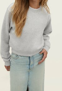 Sweatshirt gris à col rond et manches longues, associé à une jupe en denim bleu clair avec une fente sur le devant et un design classique à cinq poches.