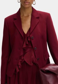 Blazer burdeos de tejido suave con un corte entallado, diseño de un solo botón, tres botones y solapas con muesca. Top fruncido debajo.