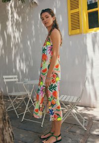 Vestito colorato senza maniche con motivi di frutta e foglie, realizzato in tessuto leggero, con spacco laterale e vestibilità ampia.