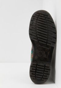 Suela de goma negra con patrón de agarre texturizado. Diseño floral colorido en el costado, que enfatiza la forma y la construcción del zapato.