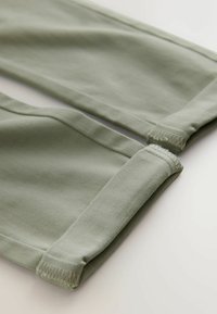 Pantaloni in cotone verde chiaro con polsini elastici, superficie liscia e design semplice con cuciture ben rifinite ai margini.