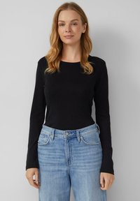 Maglietta nera a maniche lunghe in un design aderente, realizzata in un tessuto liscio. Abbinata a jeans azzurri chiari, a vita alta, leggermente sfrangiati.