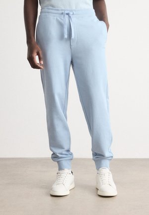 Light blue sweatpants with elastic waistband and drawstring, side pockets, and fitted cuffs. Worn with white sneakers. Smooth fabric texture.