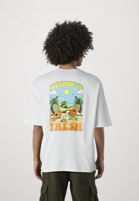 Camiseta blanca de algodón con un gráfico colorido en la parte posterior que presenta frutas de dibujos animados, elementos de playa y el texto "MANTENIÉNDOLO FRESCO."
