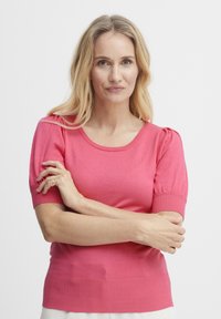 Majica s kratkimi rokavi, prilega se postavi, v svetlo roza barvi. Ribošiti robovi in rokavi s napihnjenim detajlom na ramenih. Gladka tekstura, okrogla izreza.
