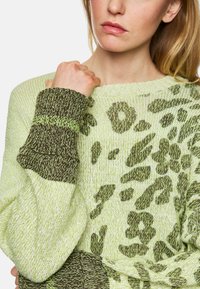 Strickpullover in Hellgrün mit einem braunen Tiermuster. Mit einem kontrastierenden, braunen, strukturierten Ärmel. Weiches, leichtes Material.