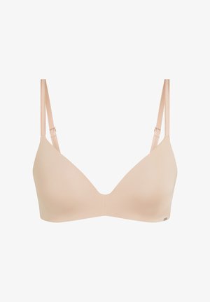 Soutien-gorge beige sans couture rembourré avec bretelles fines réglables, bonnets lisses et petit logo métallique en bas à droite.