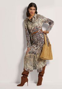 Langes Hemdkleid mit floralem und gestreiftem Muster in Beige, Blau und Braun. Brauner Gürtel, knielange braune Stiefel und eine braune Schultertasche.
