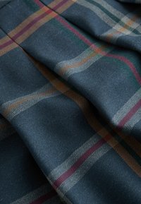 Tissu bleu foncé avec un motif à carreaux comprenant des rayures rouges, vertes, moutarde et blanches, présenté avec des plis doux et des détails de texture.