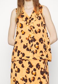 Top sans manches à imprimé léopard orange avec un avant à volants, fabriqué en tissu léger, présentant un décolleté en V et une coupe décontractée.
