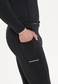 Zwarte sneldrogende sporttop met lange mouwen en een nauwsluitend ontwerp. Beschikt over een zijzak en reflecterende accenten voor zichtbaarheid.