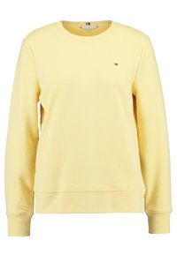 Jasnożółta bluza z okrągłym dekoltem i długimi rękawami z małym logo Tommy Hilfiger po lewej stronie klatki piersiowej.