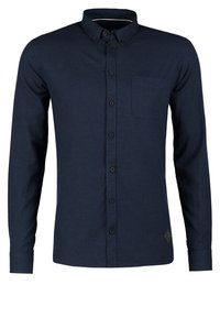Chemise bleue marine à manches longues avec poche poitrine et col à boutons, présentée sur un fond blanc uni.