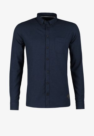 Man walking, wearing a dark shirt and black pants, holding a black leather briefcase in his left hand.