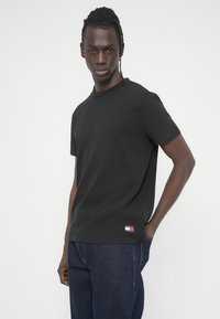 Μαύρο T-shirt με κοντά μανίκια και ριμπ υφή, με στρογγυλή λαιμόκοψη. Διαθέτει μικρό λογότυπο σε κόκκινο, λευκό και μπλε στο τελείωμα.