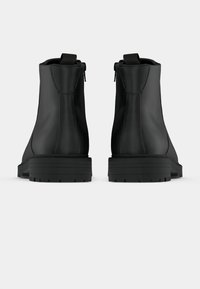 Botines negros con acabado de cuero liso, cremalleras laterales y suelas de goma gruesa con un patrón estriado para mayor tracción.