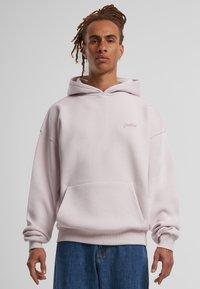 Haut à capuche rose clair avec poche avant, poignets côtelés et détail de logo sur la poitrine. Tissu doux avec une coupe décontractée. Assorti avec un jean bleu.