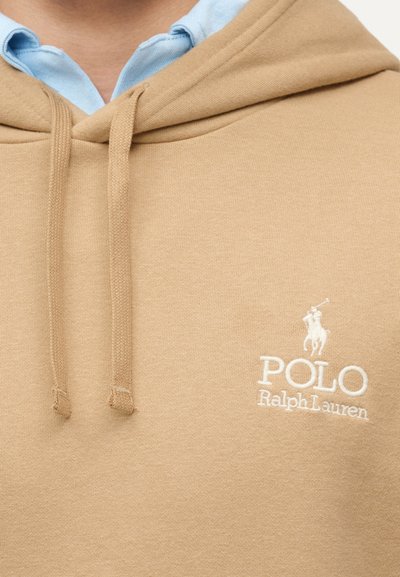 Μπεζ φούτερ με κορδόνια που φοριέται πάνω από ανοιχτό μπλε πουκάμισο με γιακά, με λευκό λογότυπο Polo Ralph Lauren στο στήθος.
