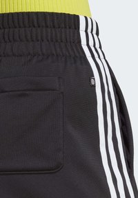Černé sportovní šortky s bílými bočními pruhy, elastickým pasem a zadní kapsou. Hladká textura látky s logem na boku.