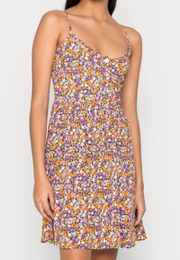 Blumenkleid mit einem lila, orange und weißen Muster, Spaghettiträgern und einer Knopfdetaillierung auf der Vorderseite. Leichter Stoff.