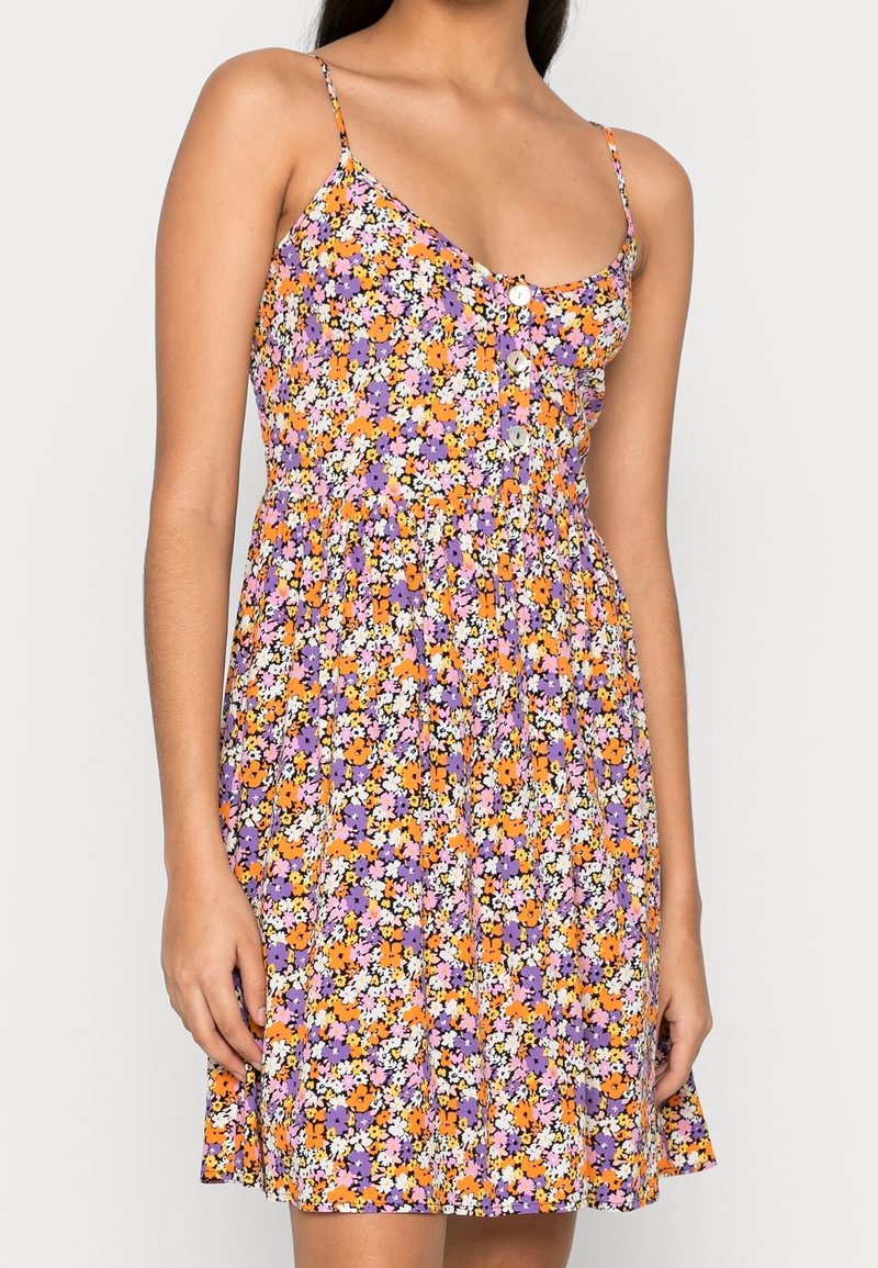 Blumenkleid mit einem lila, orange und weißen Muster, Spaghettiträgern und einer Knopfdetaillierung auf der Vorderseite. Leichter Stoff.