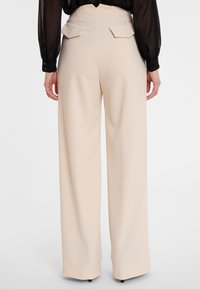 Beige wijde broek met een gladde textuur, hoge taille en twee achterzakken met flapdetails. Gecorrigeerd, losvallend ontwerp.