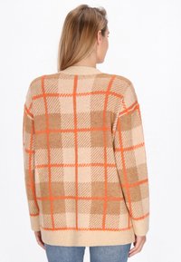 Maglione beige con un motivo scozzese arancione e marrone. Il design include un collo a giro e una vestibilità ampia, con polsini e orlo a coste.