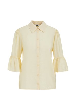 Blouse crème avec boutonnage sur le devant, col pointu, et manches trois-quarts bouffantes se terminant par des poignets à volants.