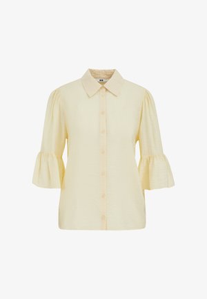 Kremasta bluza z gumbi na sprednji strani, koničastim ovratnikom in rokavi tri četrtine dolžine z nabranimi manšetami.