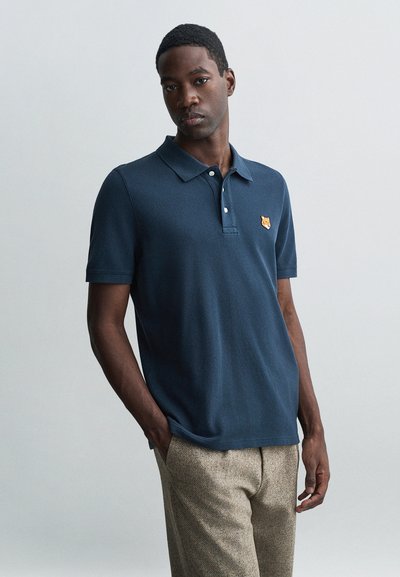 Polo shirt bleu marine foncé avec une finition texturée, comportant une patte de boutonnage à trois boutons et un petit logo d'ours brodé sur la poitrine.