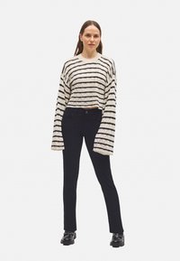 Suéter de ganchillo con rayas negras sobre una base blanco roto, combinado con pantalones ajustados negros y zapatos negros gruesos.