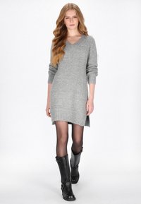 Rochie tricotată gri cu decolteu în V, manșete cu nervuri și o margine din spate ușor mai lungă, asortată cu cizme negre din piele până la genunchi.