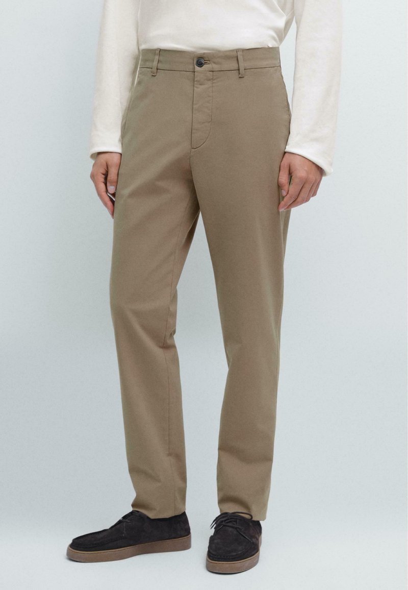 Khaki-Chinos aus Baumwollmischung, gerades Bein, mittelschwerer Stoff, mit Einknopfverschluss, seitlichen Taschen, getragen mit dunklen Wildlederschuhen.