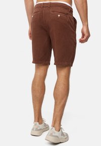 Shorts marron en tissu doux, dotés de deux poches arrière avec boutons et d'un ourlet décontracté. Assortis à des baskets de couleur claire.