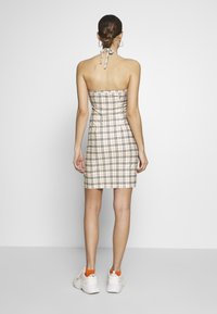 Beżowa sukienka bodycon bez ramiączek w czarny wzór w kratę, z dopasowanym krojem i zawiązywanym na szyi halter. Noszona z białymi trampkami.