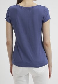 Kortärmad t-shirt med rund halsringning i djupblått tyg. Slät textur, åtsittande design, synlig söm vid axlarna, bärs med vita jeans.