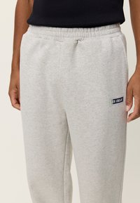 Ανοιχτόγριες φόρμες από απαλό υλικό με ελαστική μέση, με μικρό μπλε και πράσινο λογότυπο.