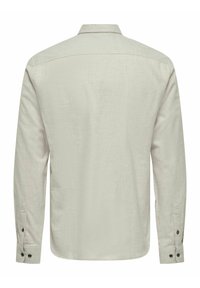 Camisa de manga larga de color beige claro, confeccionada con una tela texturizada, que presenta un cuello clásico y puños abotonados. Diseño simple y limpio con un corte relajado.