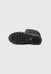 Botte en caoutchouc noire avec une surface texturée, un motif de semelle en zigzag et un accent de fermeture éclair doré sur le côté. Conception durable et résistante aux intempéries.