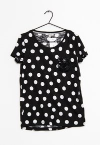 Camiseta negra de manga corta con lunares blancos y un bolsillo de lentejuelas negras texturizadas. Cuello redondeado y tejido suave.