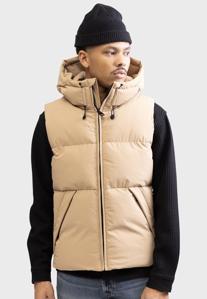 Chaleco acolchado beige con cuello alto y capucha, que cuenta con un cierre frontal, dos bolsillos delanteros y cordones ajustables para un mejor ajuste.
