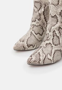 Botines de punta puntiaguda en beige con textura de estampado de serpiente marrón, con un diseño ajustado y superficie lisa con un brillo sutil.