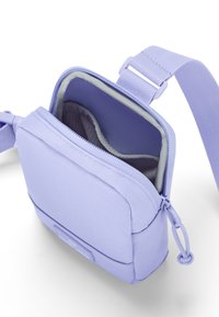 Lila tygaxelväska med en dragkedjeförsedd huvudficka, vadderad innerficka och justerbar rem. Slät textur och lättviktsdesign.