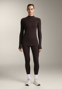 Completo sportivo bordeaux composto da una maglia a maniche lunghe con zip e leggings abbinati. Texture liscia con design aderente.
