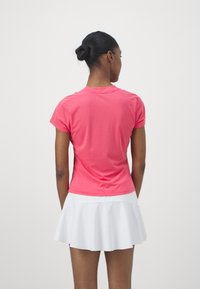 Top atlético rosa de manga corta con cuello redondo, de textura suave, combinado con una falda blanca de corte acampanado. Visto desde la parte de atrás.