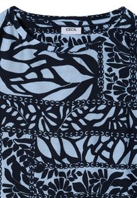 Chemise en tissu bleu clair avec motif abstrait floral noir et motif en forme de chaîne, col rond, et étiquette de marque "CECIL" à l'intérieur du col.