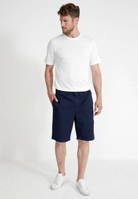Miesten valkoinen crew-neck t-paita yhdistettynä tummansinsisiin shortseihin. Shortseissa on joustava vyötärö ja taskut; molemmat vaatteet ovat rentoja ja kevyitä.