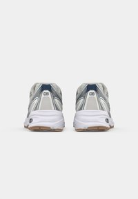 Un par de zapatillas deportivas grises y marino vistas desde la parte trasera, con mediasoles blancos y suelas marrones sobre un fondo blanco.